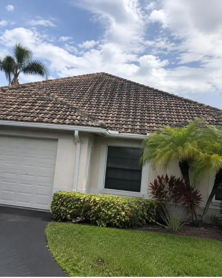 A barrel tile roof almost black with algae above a beige house and garage.
