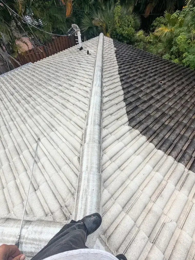 A concrete tile roof mid-clean. Most of the roof is now pale grey and clean while a section of the far slope remains dark with algae growth.
